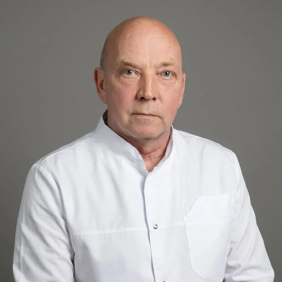 Portrait of a middle-aged bald man in a white shirt looking at the camera against a gray background.