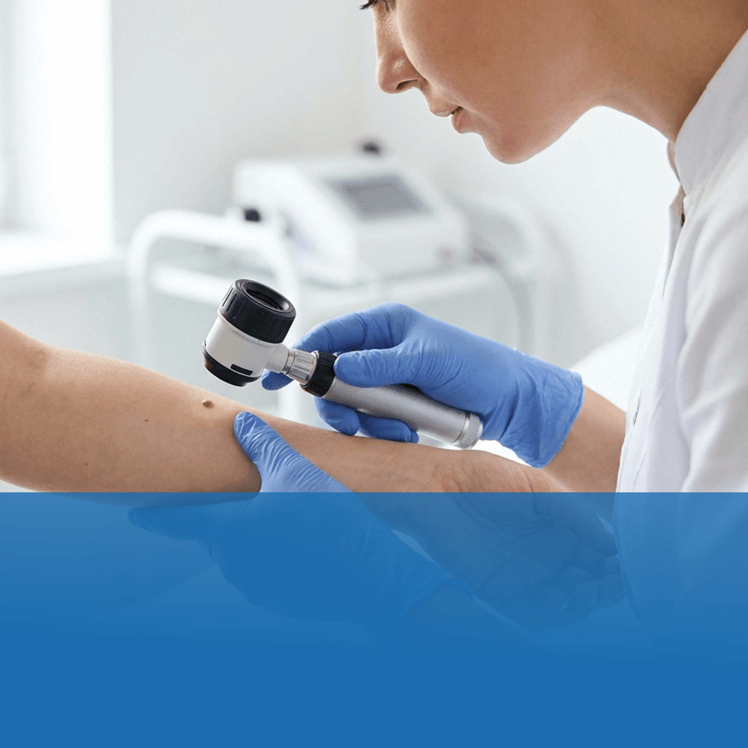 Healthcare professional wearing blue gloves examines a forearm with a dermatoscope.